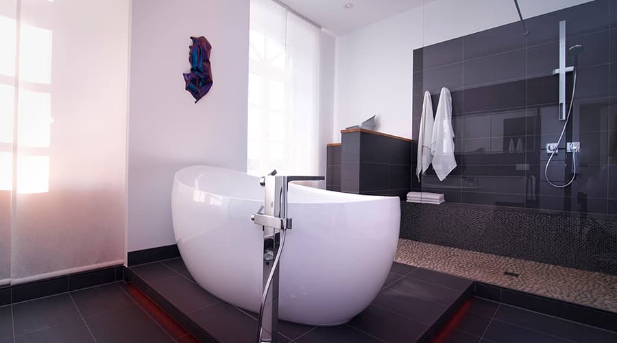 Renoviertes Badezimmer mit großen schwarzen Fliesen und freistehender Badewanne