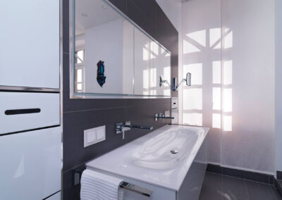 Modernes, helles Badezimmer mit Waschtisch, wandmontierter Armatur und großem Spiegelschrank