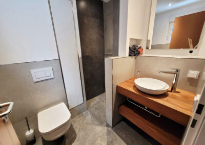 Modernes Badezimmer mit bodengleicher Dusche, wandhängendem WC und Waschtisch mit Holzoberfläche